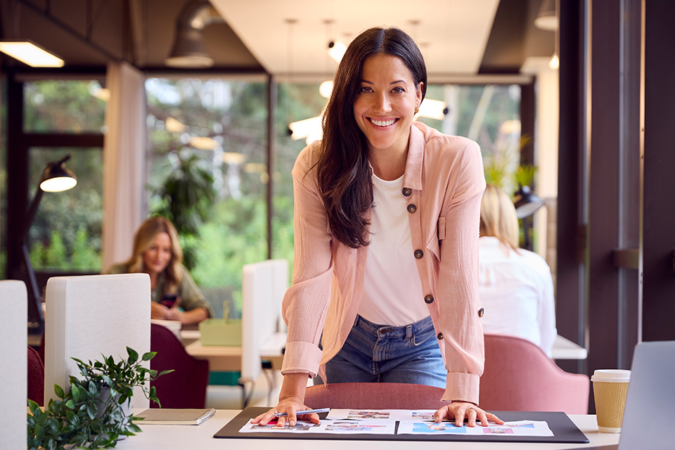 Female business administration professional smiles at camera while working at desk in office setting.