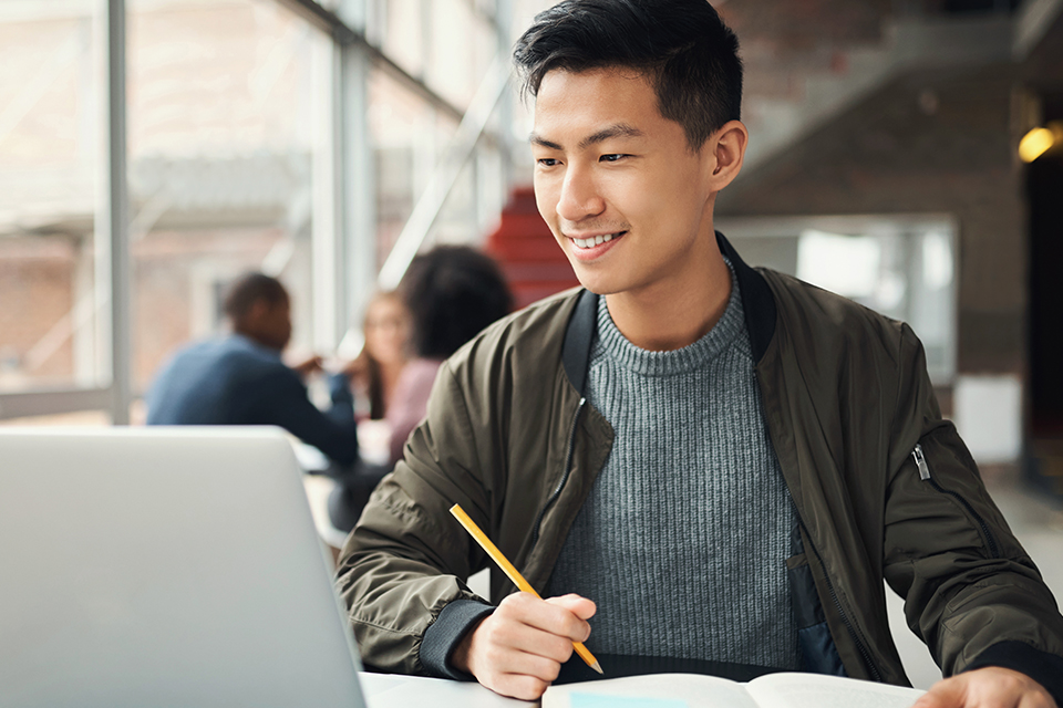 Student working on online business degree on laptop in an open area.