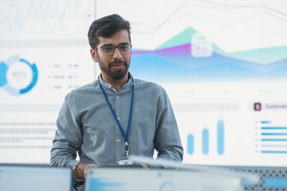 Man Presents Information with Data Charts Behind Him