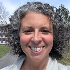 Donna Dolansky with shoulder length curly air stands on campus and smiles at the camera.