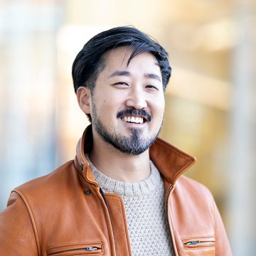 Jason Koo, in beige sweater and orange jacket, smiles at the camera.