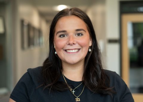 Megan Chamberlain with shoulder-length dark hair and black spot smiles at camera.