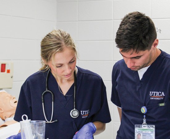 Nursing students in scrubs, look over paperwork near a mock-patient.